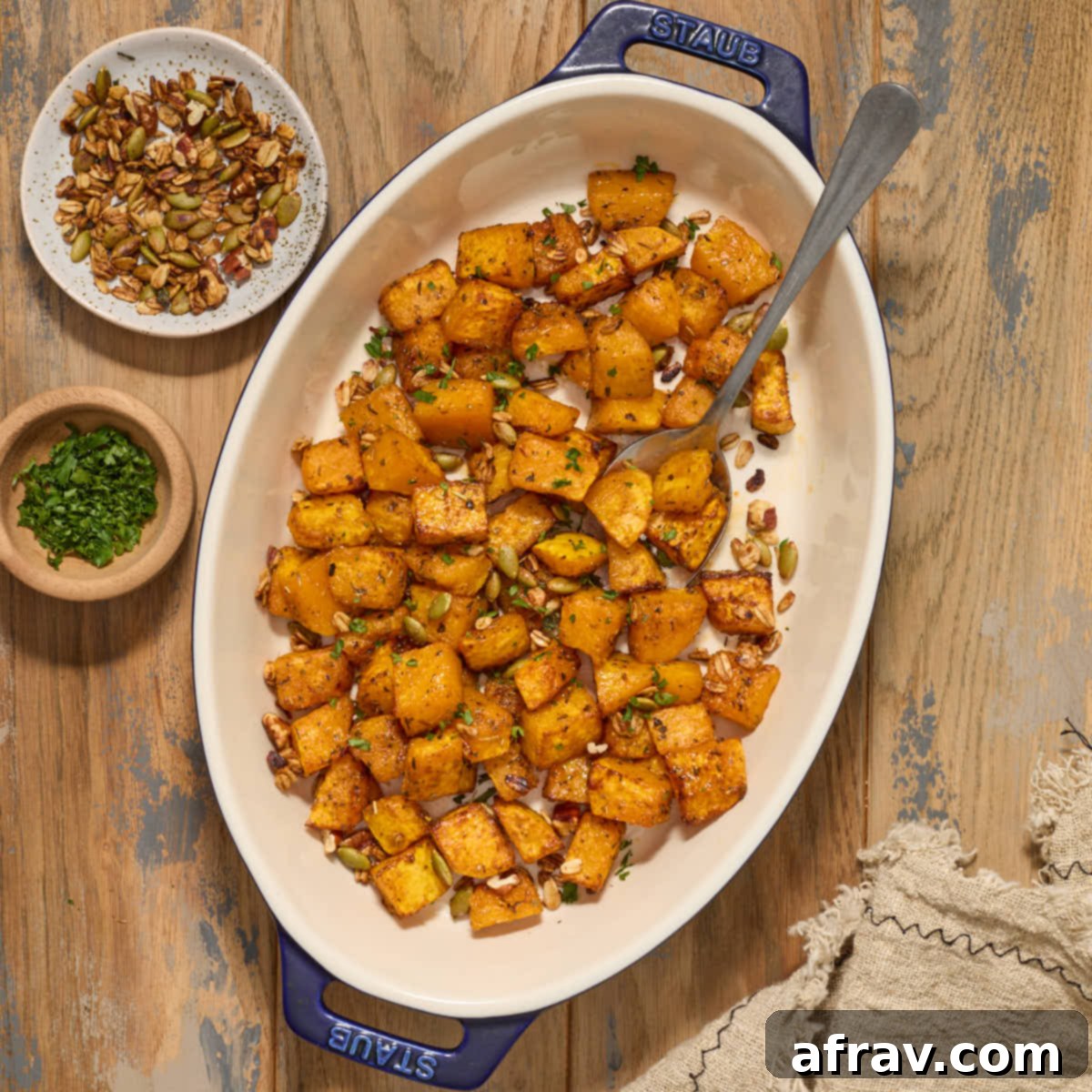 Effortless Air Fryer Side Dishes 4 Air fryer butternut squash cubes in a serving dish with chopped pecans, pumpkin seeds and fresh herbs, showcasing a perfect fall side.