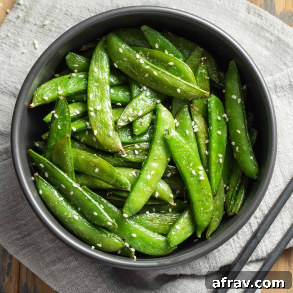 Effortless Air Fryer Side Dishes 6 Overhead view of air fryer snap peas in a black bowl on top of a grey napkin, showing their fresh green color.