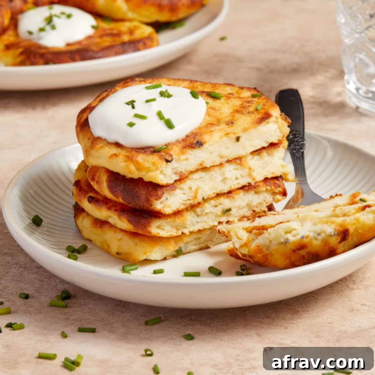 Effortless Air Fryer Side Dishes 8 Stack of air fryer potato cakes on a plate with a dollop of sour cream and chopped chives on top, looking comforting and delicious.