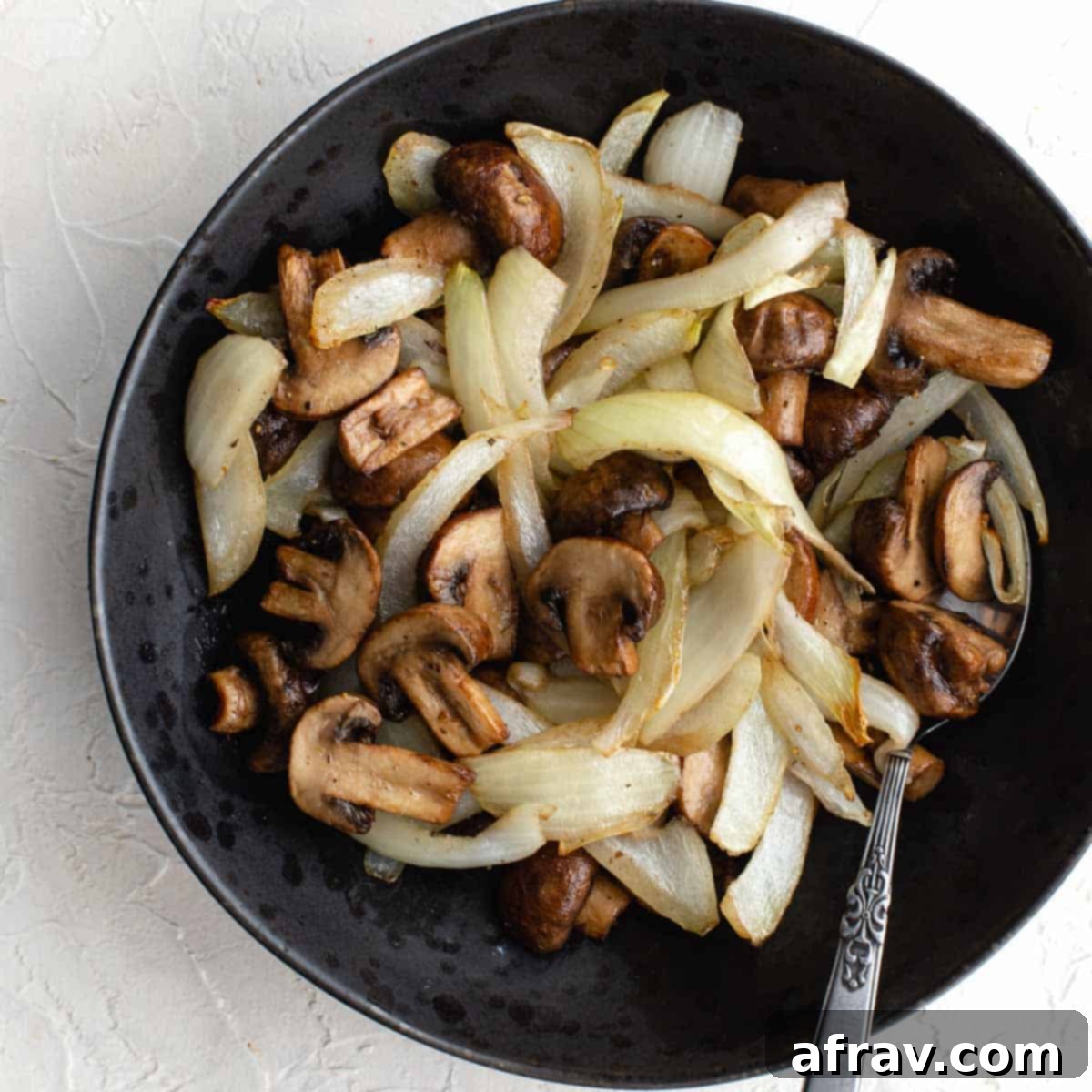Effortless Air Fryer Side Dishes 10 Air fried mushrooms and onions served in a black bowl with a spoon, looking perfectly caramelized.