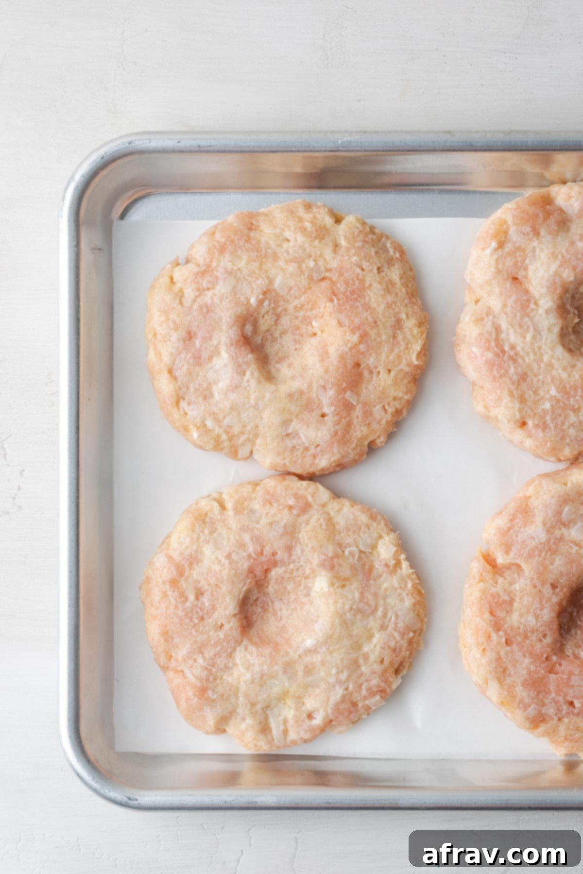 Perfectly Juicy Air Fryer Turkey Burgers 6 Turkey burger patties on a baking sheet lined with parchment paper.