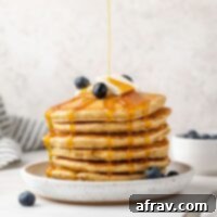 Syrup being poured over a stack of oat flour pancakes topped with blueberries.