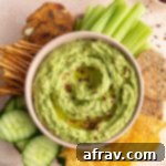 Overhead view of arugula hummus in a bowl with crackers and vegetables surrounding it.
