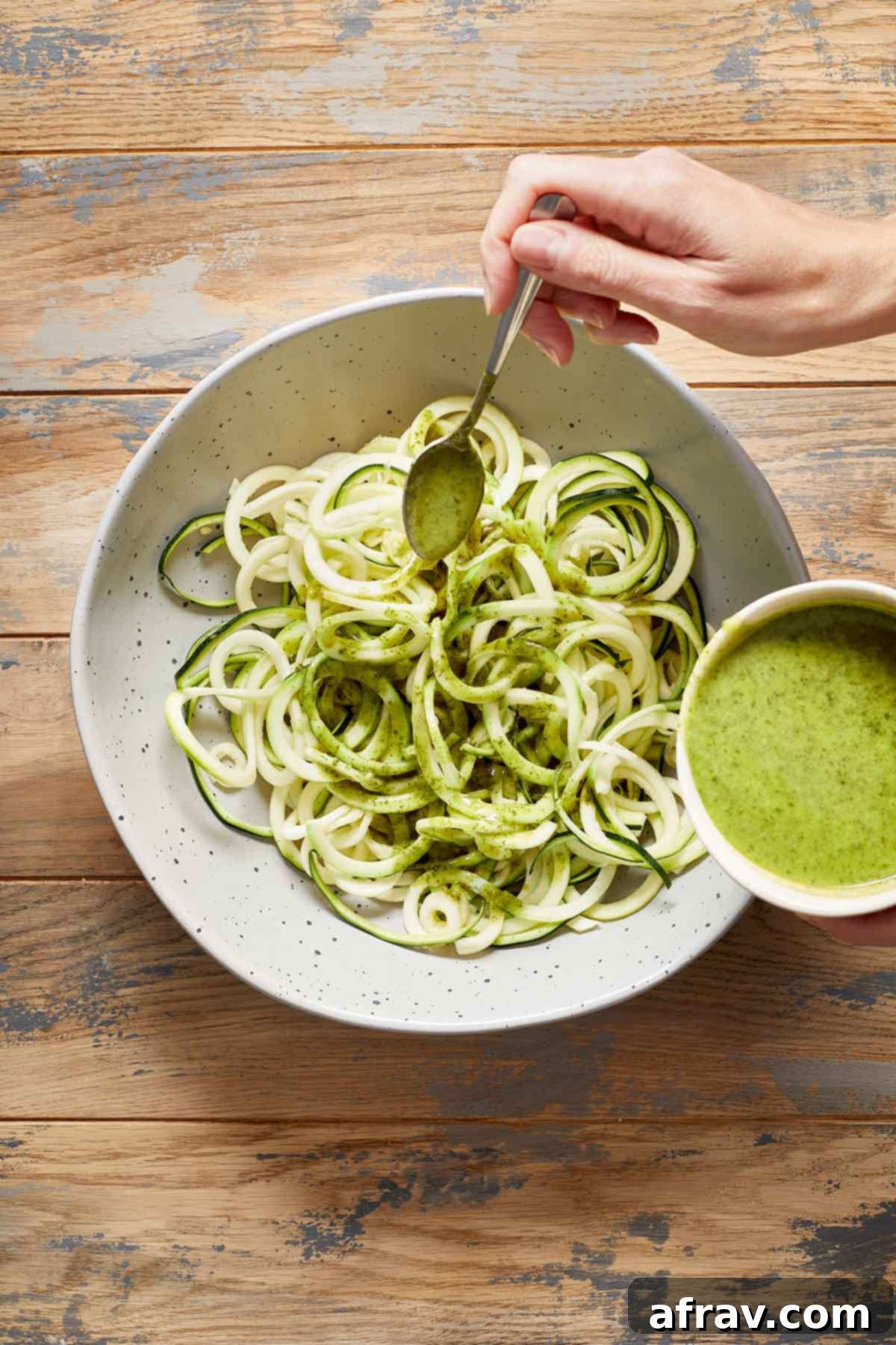 Zoodle Bowls 5 Zucchini noodles in a large bowl with jalapeño vinaigrette being drizzled over them with a spoon.