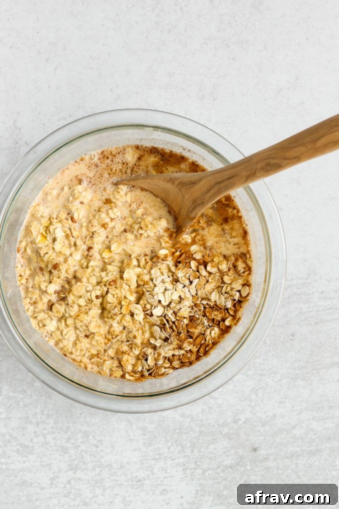 Overhead view of wet ingredients being whisked into the center of the oat mixture in a glass mixing bowl
