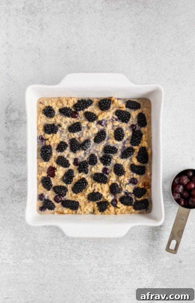 Overhead view of the berry oatmeal mixture in a white square baking dish before being baked, topped with blackberries