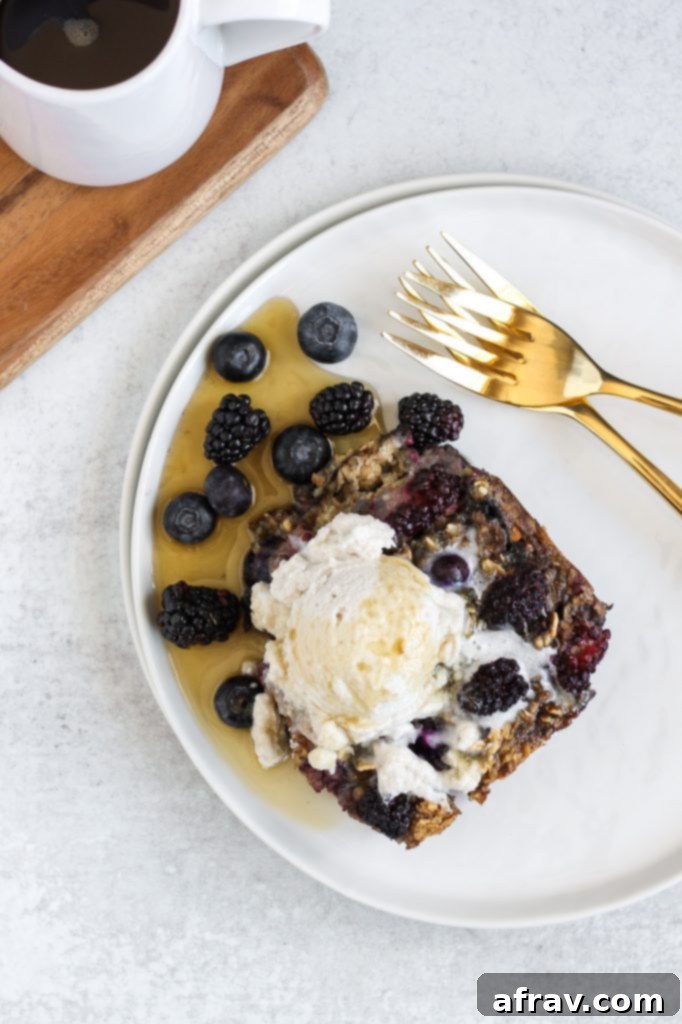 A close-up of a serving of baked berry oatmeal, generously topped with fluffy coconut whipped cream and a delicate drizzle of maple syrup