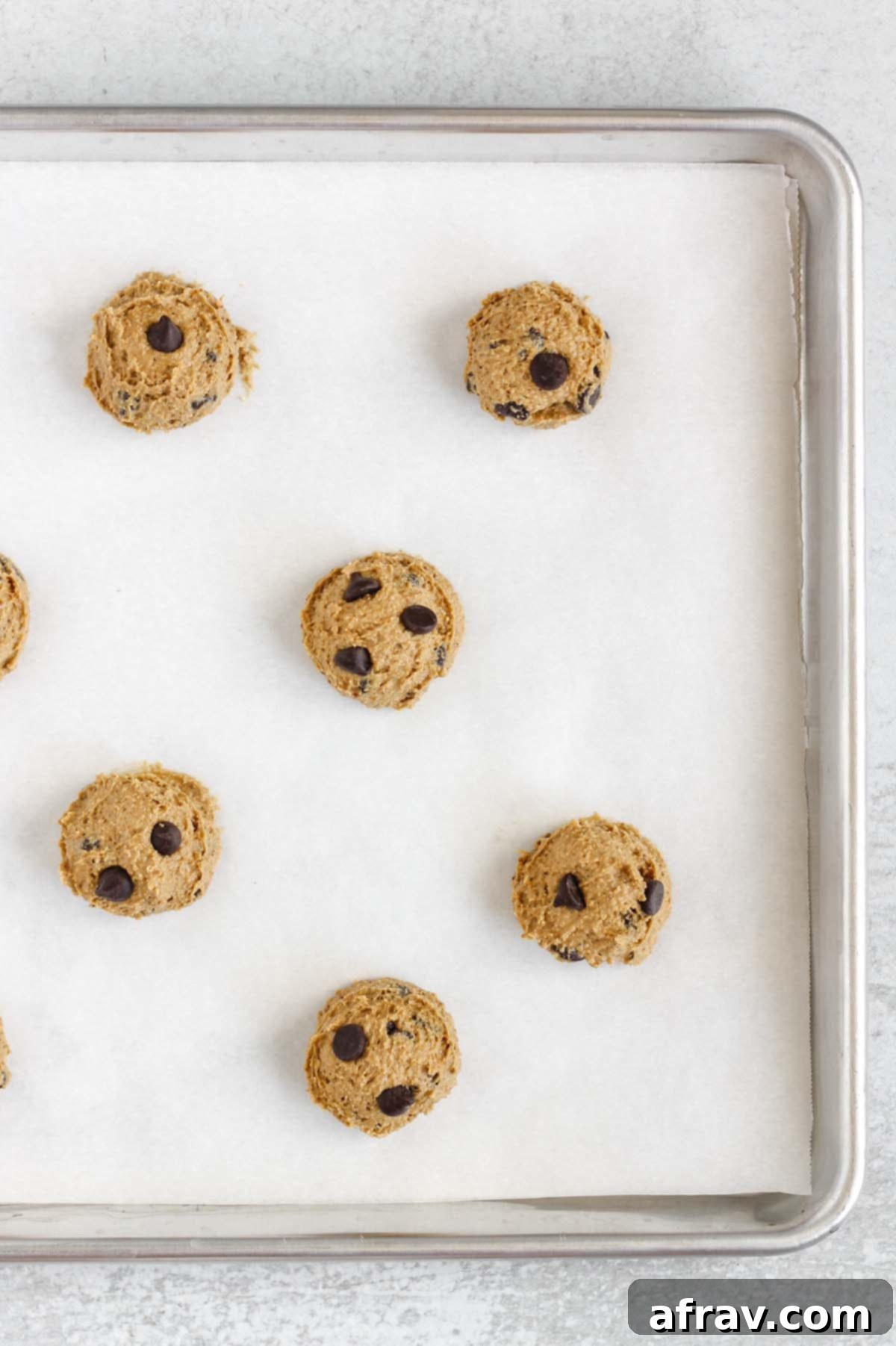 Chocolate chip cookie dough balls on a baking sheet with white parchment paper.