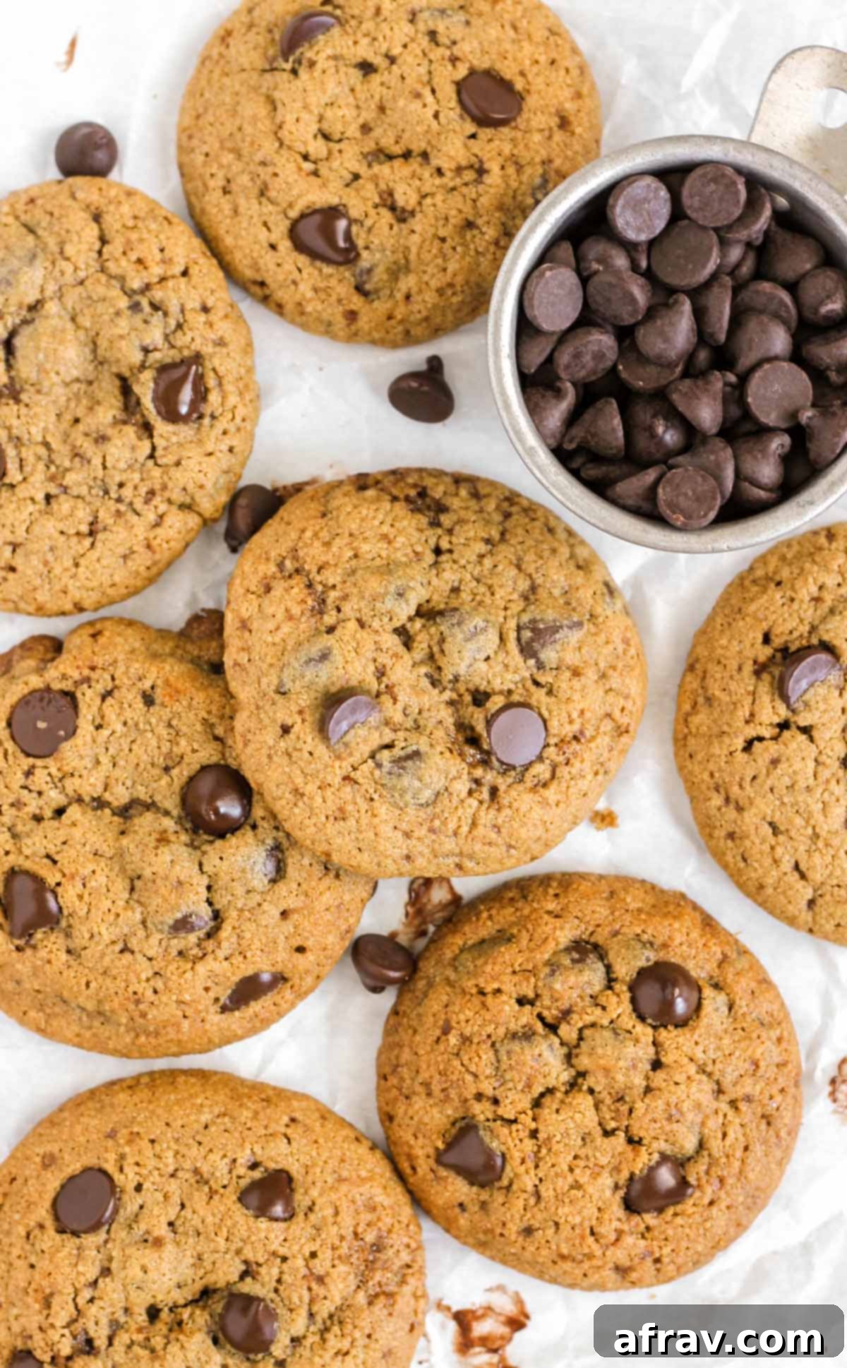 Chocolate chip oat flour cookies laid out on white parchment paper with a side dish filled with chocolate chips.