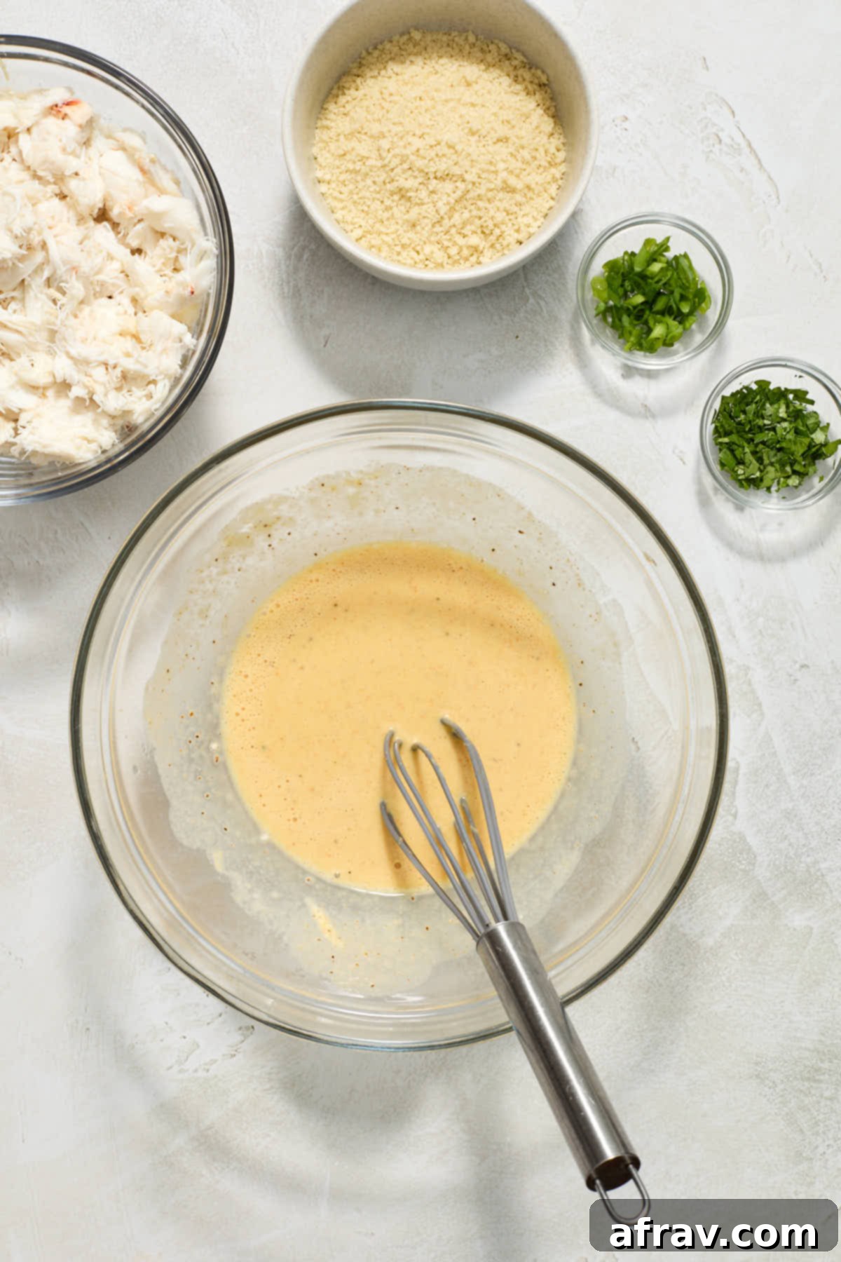 Crispy and Delicious Air Fryer Crab Cakes 4 Wet ingredients whisked together in a glass bowl with crab and other ingredients on the side, ready to be combined.
