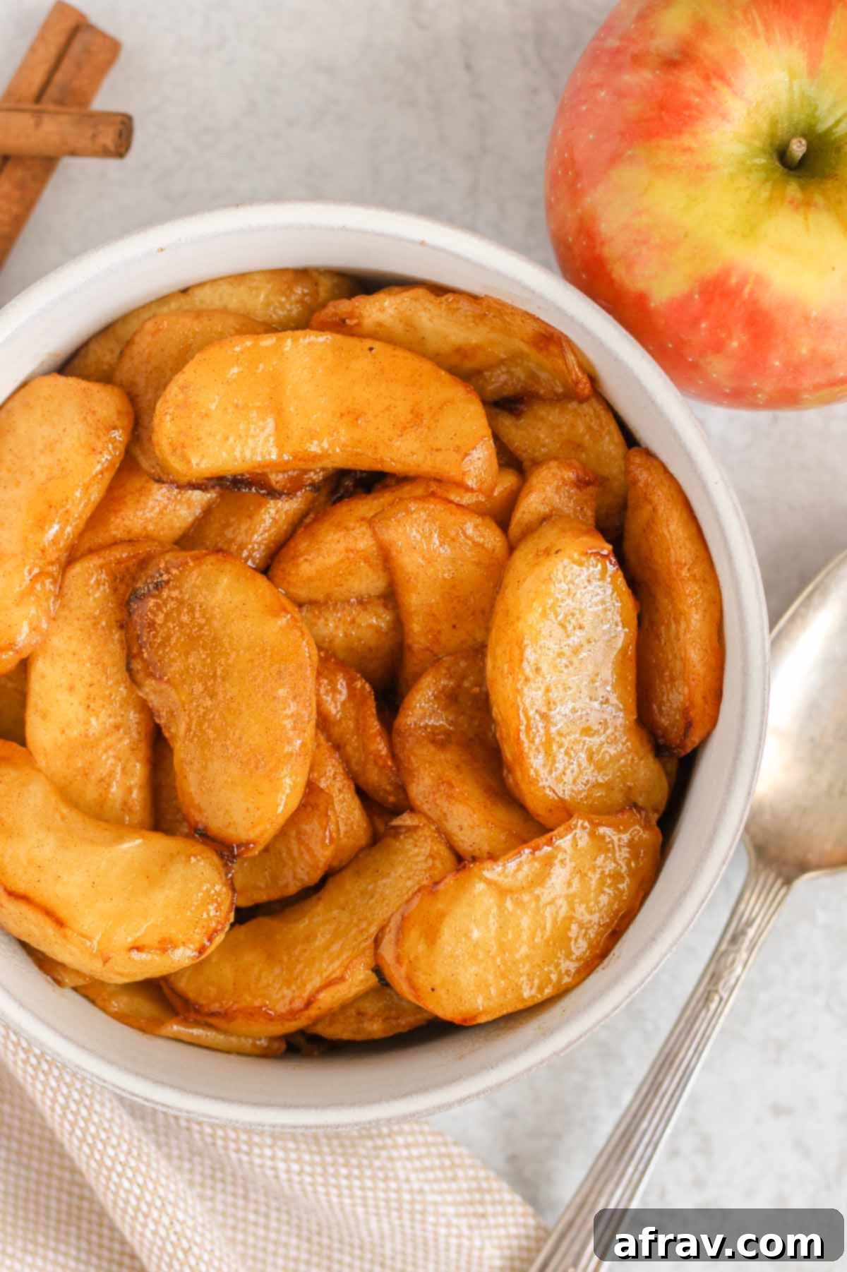 Air fried apples sprinkled with cinnamon in a serving bowl with a vintage serving spoon and apple next to the bowl.