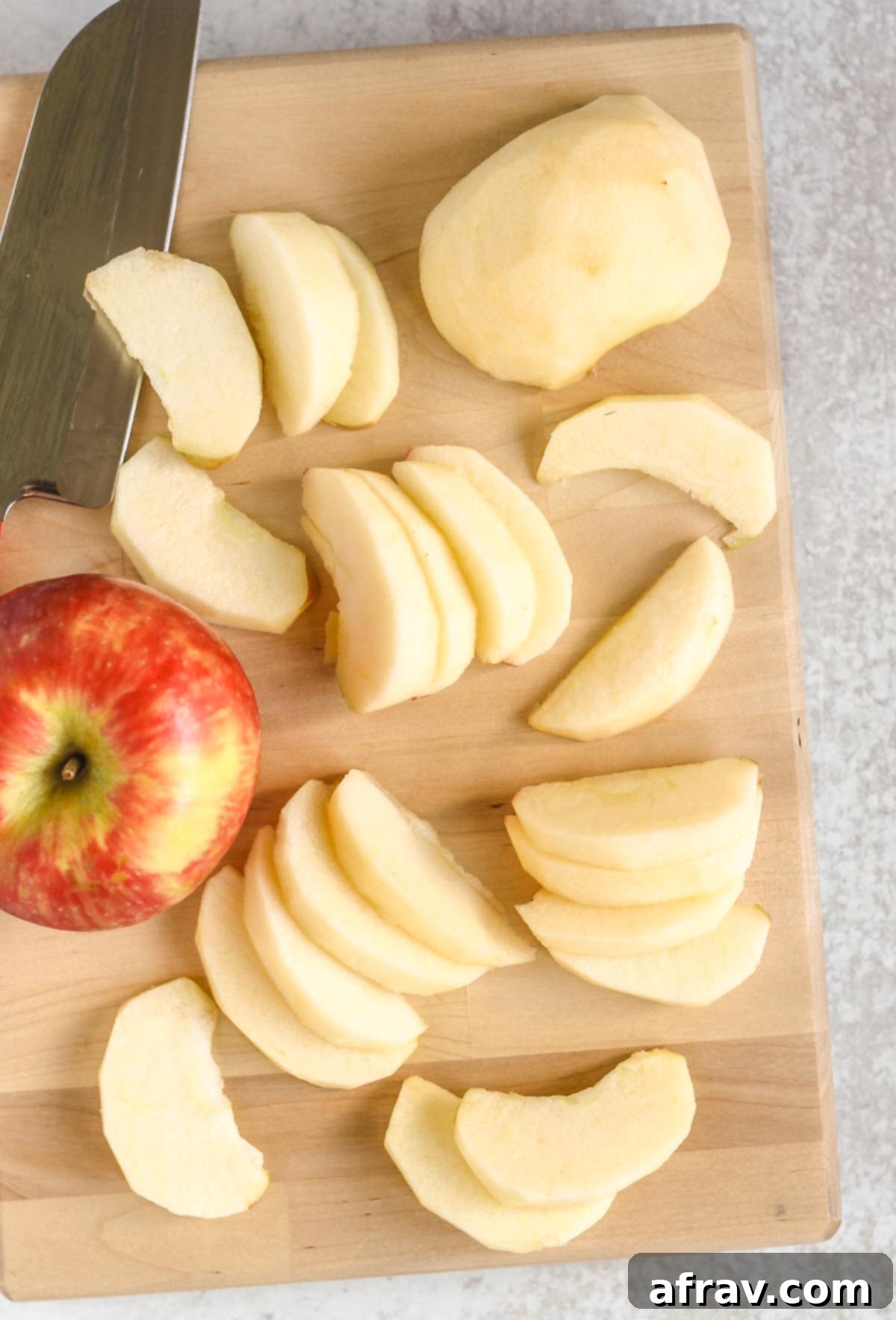Peeled and sliced apples on a cutting board with a knife and a whole apple on the side, ready for air frying.