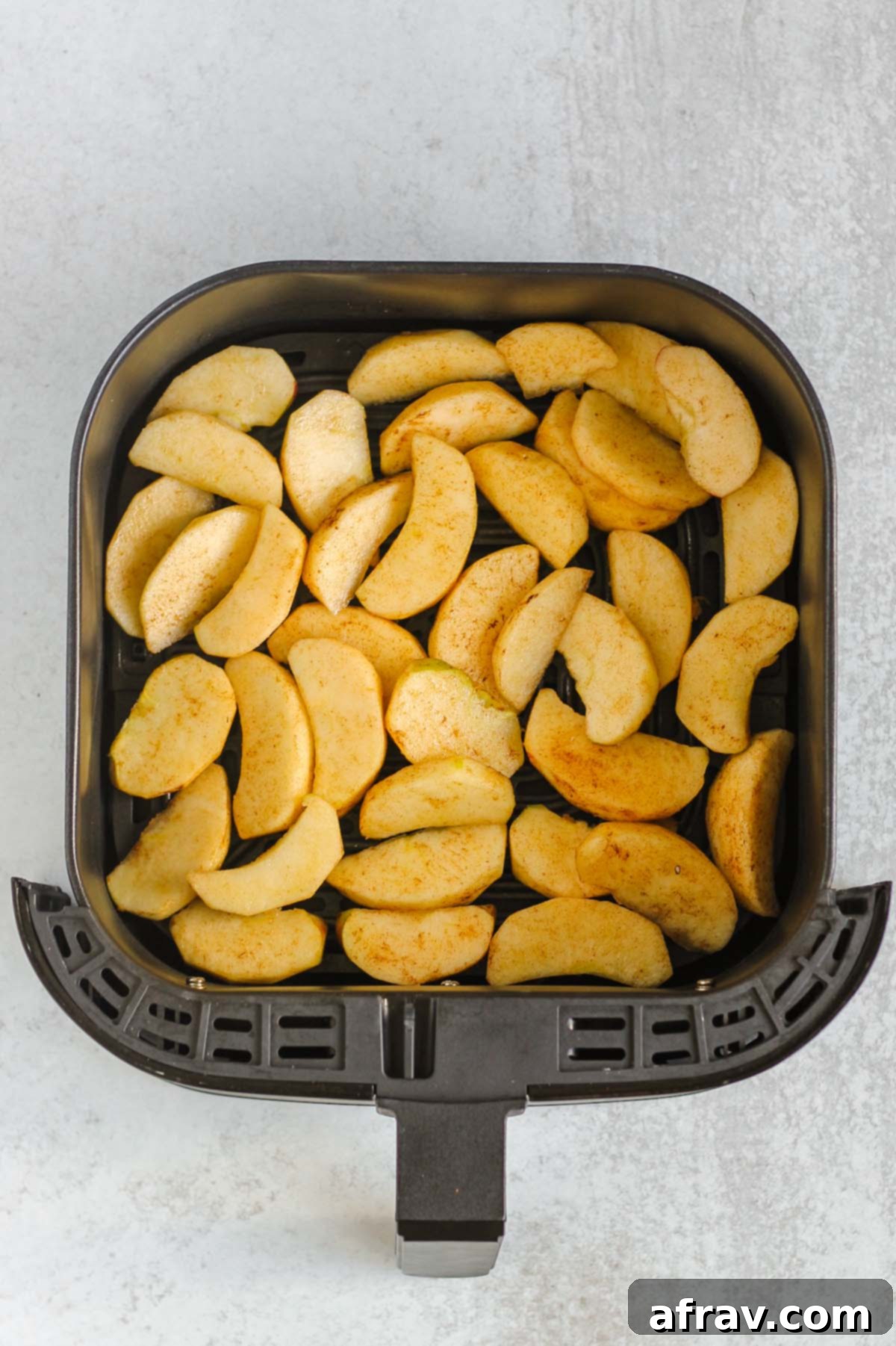 Cinnamon-coated apple slices neatly arranged in a single layer in an air fryer basket, ready for cooking.