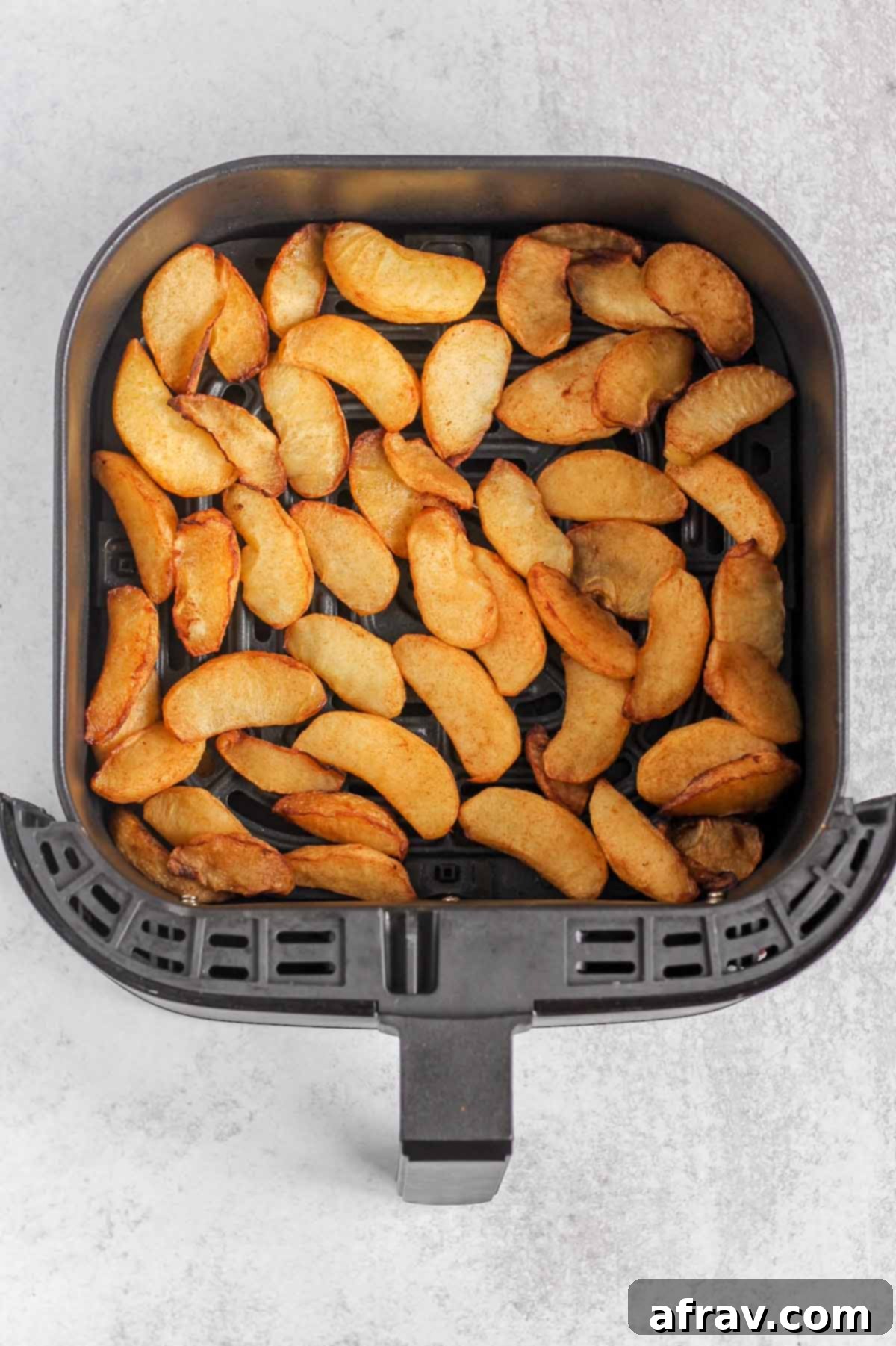 Perfectly air fried apples, golden brown and tender, shown in the air fryer basket immediately after cooking.