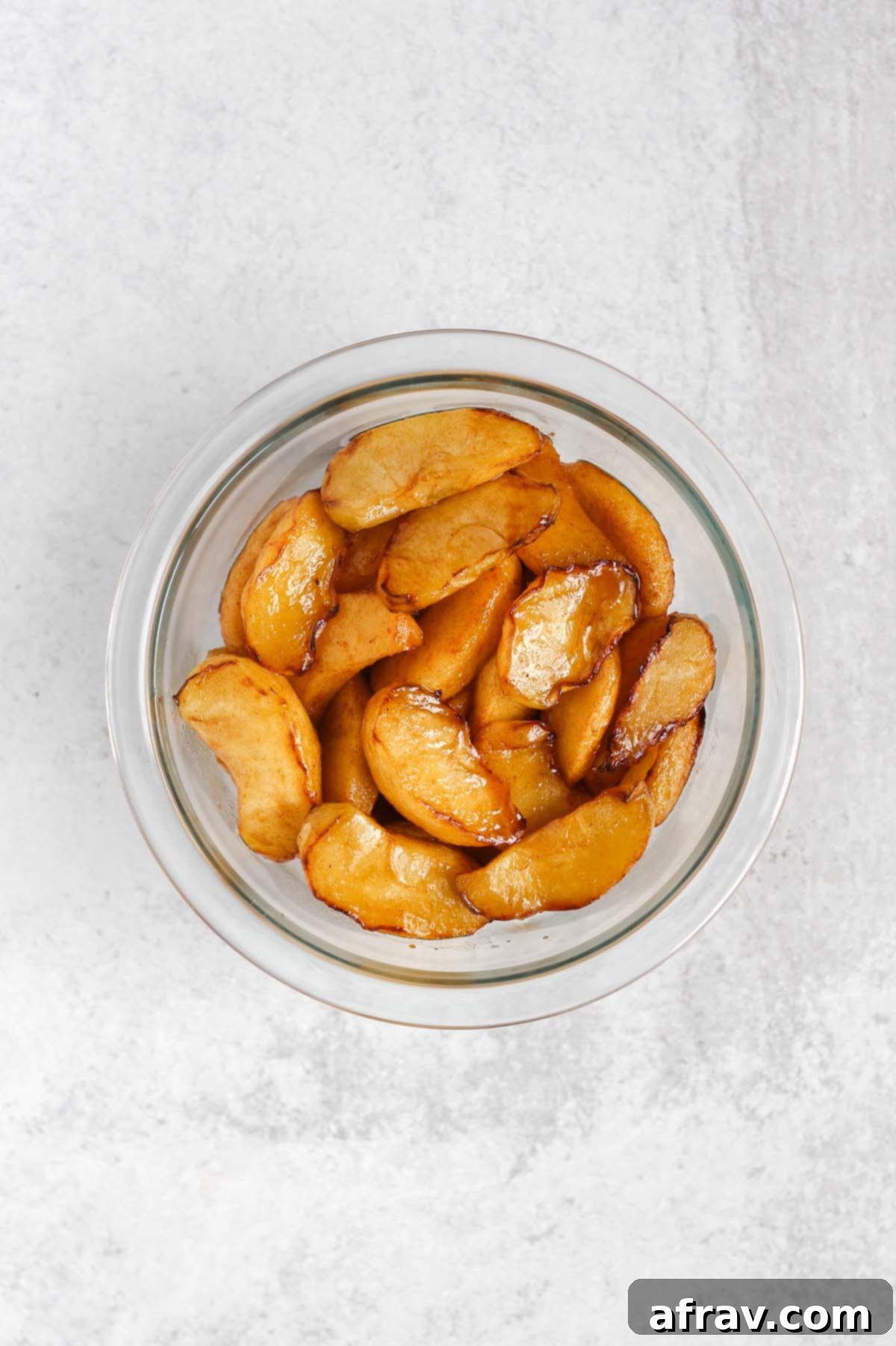 Air fried apple slices tossed with a sweet maple syrup and coconut sugar glaze in a clear glass mixing bowl.