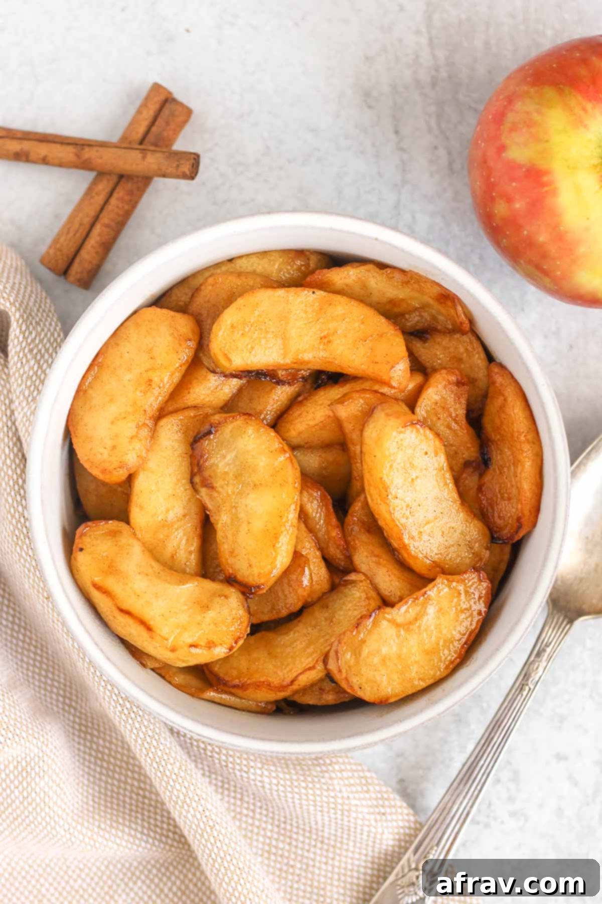 Air fried apples in a rustic serving bowl with a tan linen napkin and vintage spoon, ready to be enjoyed.