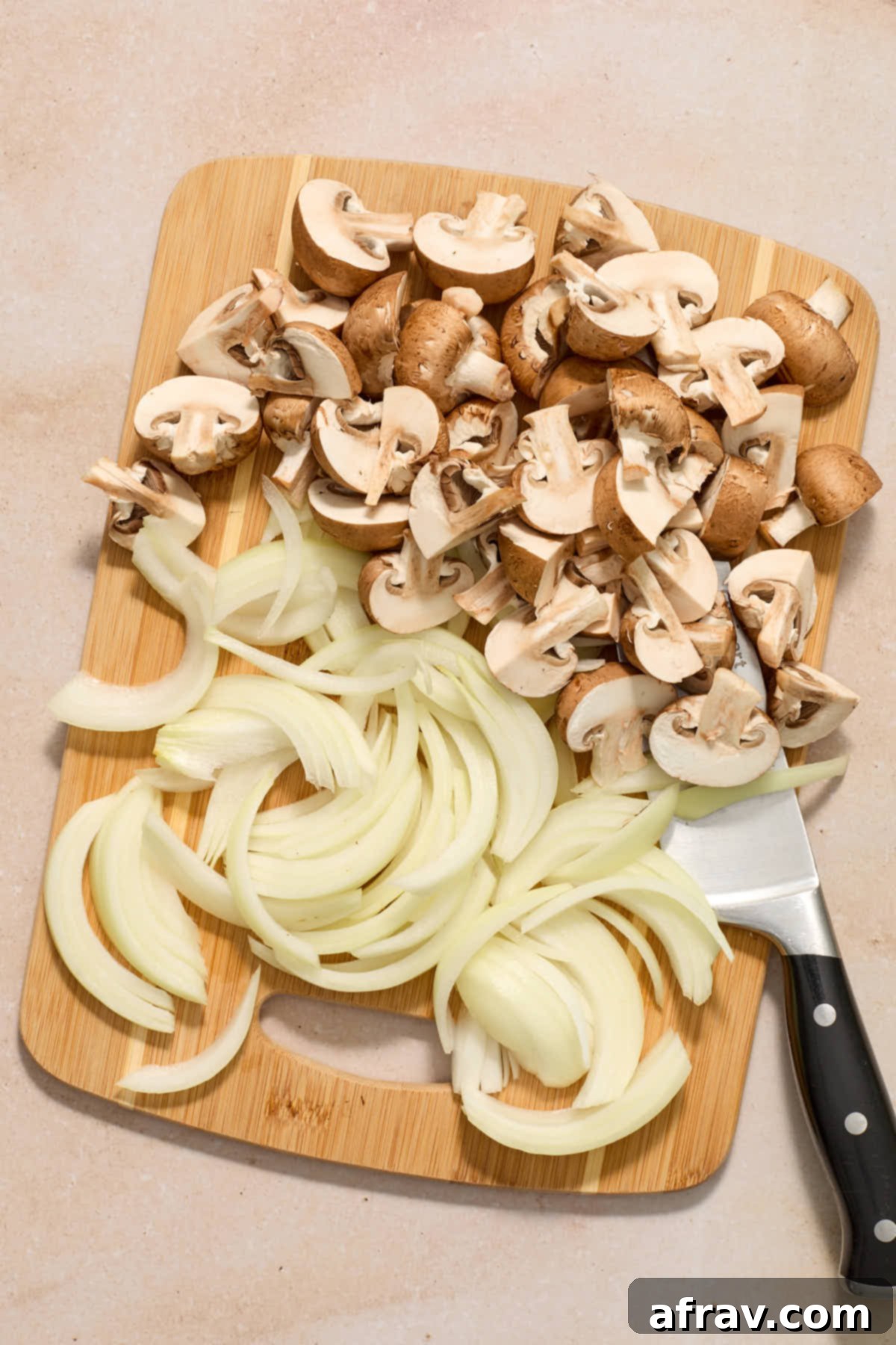 Crispy Air Fryer Mushrooms and Onions 4 Chopped mushrooms and sliced onions on a wooden cutting board with a knife.