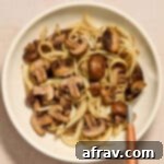 Crispy Air Fryer Mushrooms and Onions 9 Air fryer mushrooms and onions served in a white bowl with a serving spoon inserted into it.