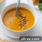 Roasted sweet potato and carrot soup in a white bowl and topped with chopped cilantro and chickpeas.