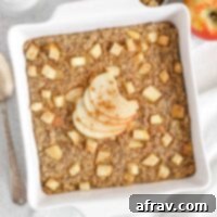 Baked apple oatmeal topped with apple slices in a square white baking dish with apples and syrup on the side.