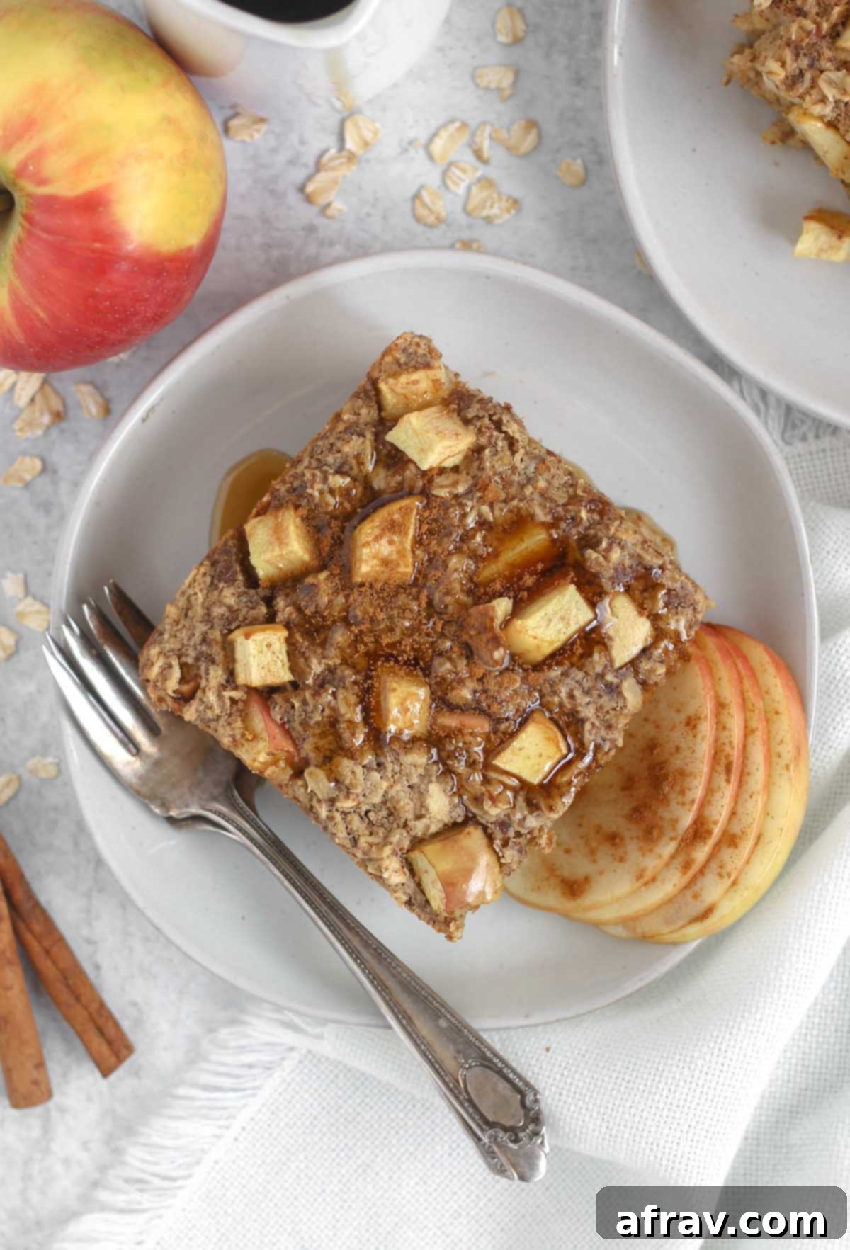 Square piece of apple cinnamon baked oatmeal topped maple syrup on a round plate with a vintage fork.