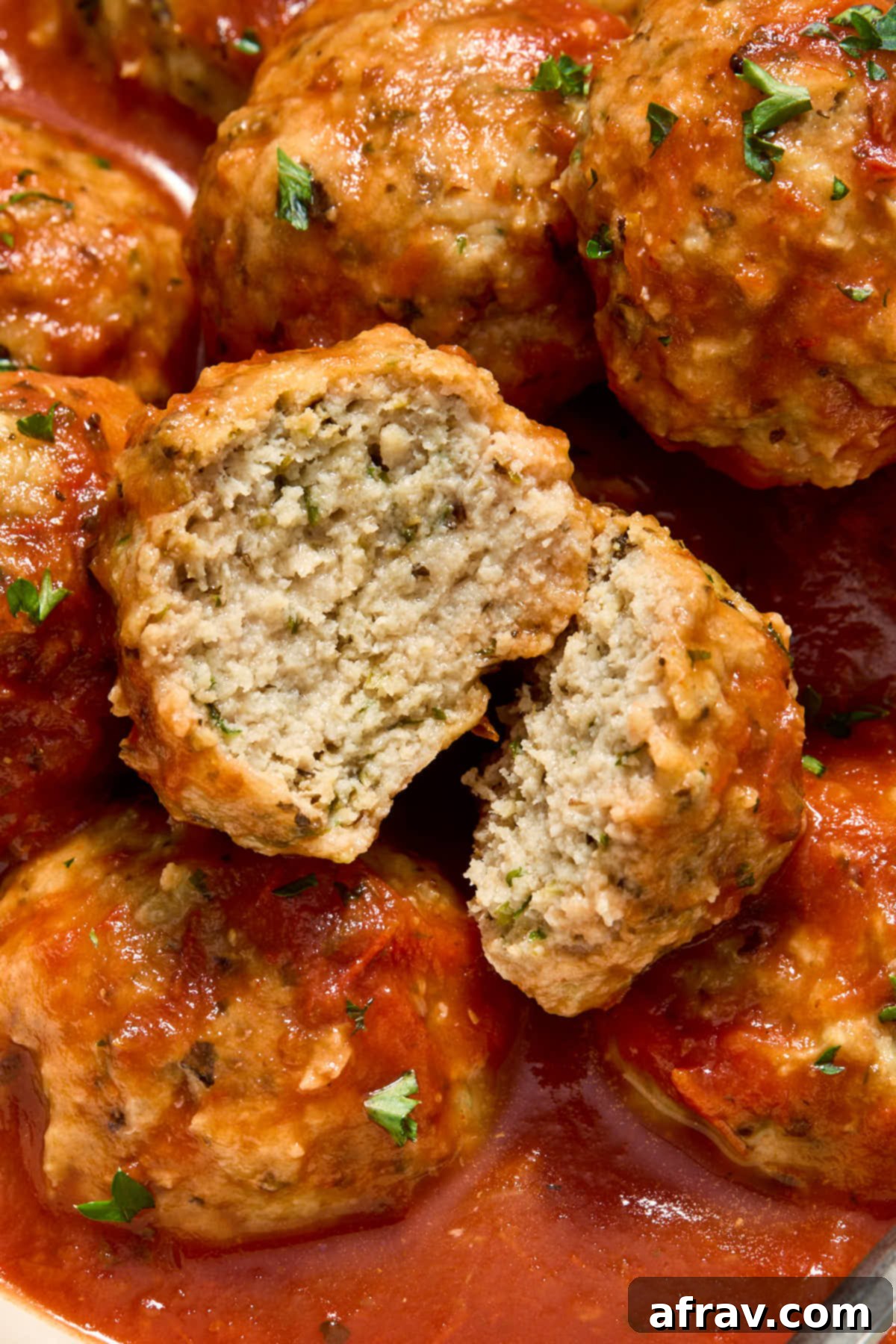 A meatball cut in half on top of a bowl of meatballs covered in marinara.