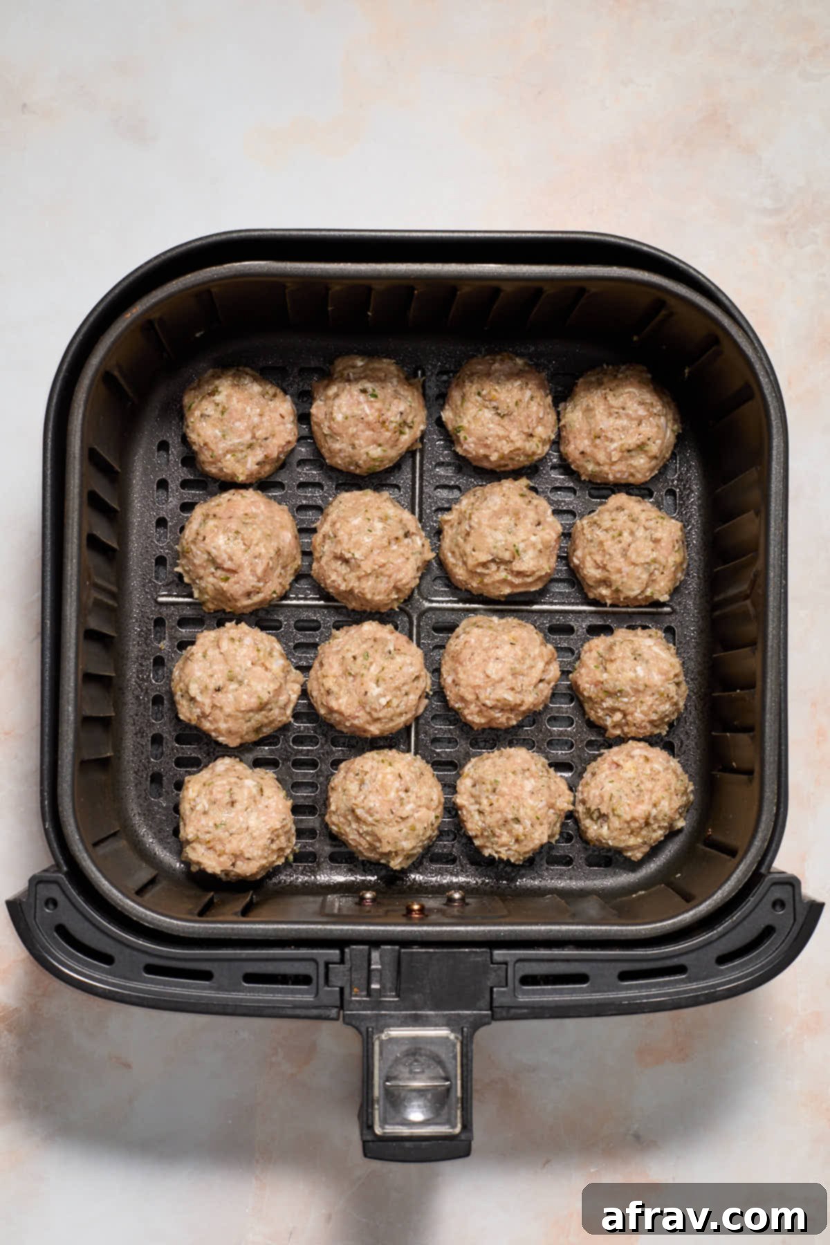 Uncooked meatballs arranged in a single layer in the air fryer basket.