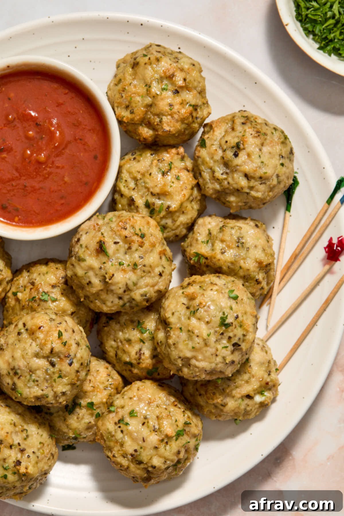 Meatballs arranged on a white plate with a small dish of marinara and toothpicks for serving.