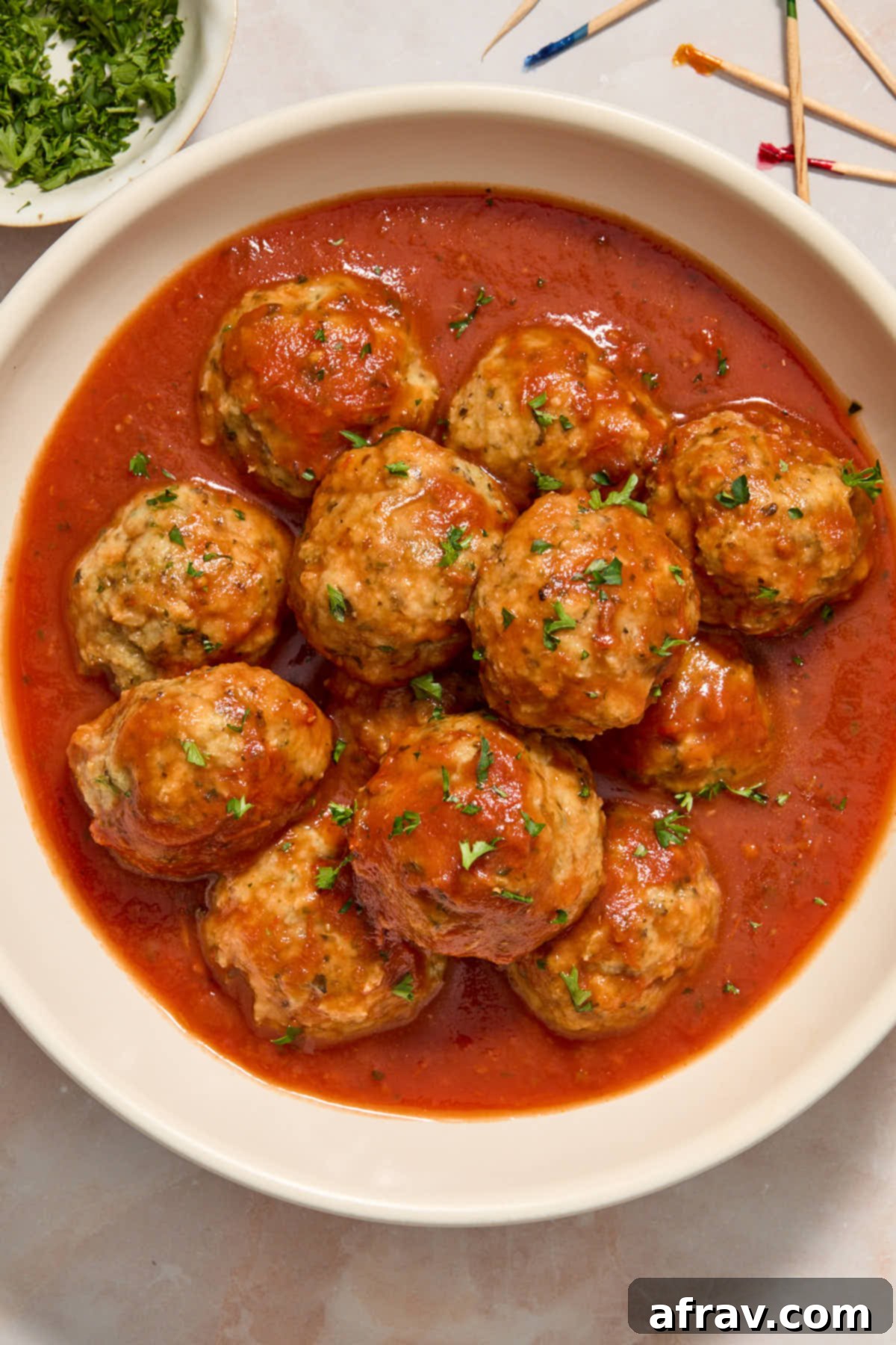 Chicken meatballs in a white bowl and covered in marinara sauce.