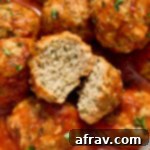 Close up of a chicken meatball cut in half on top of more meatballs topped with marinara.