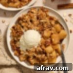 Almond flour apple pecan crisp served on a plate with a spoon and scoop of ice cream.