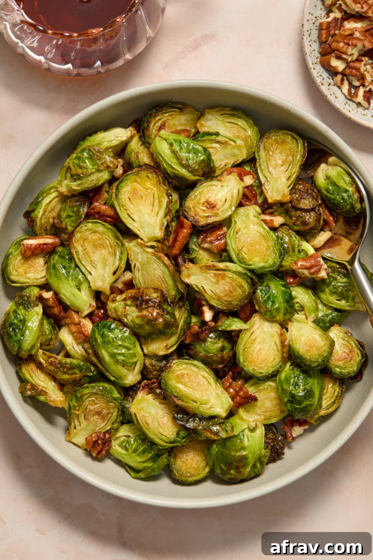 Brussels sprouts and pecans served in a grey bowl with chopped pecans and maple syrup on the side, highlighting the dish's delicious presentation.