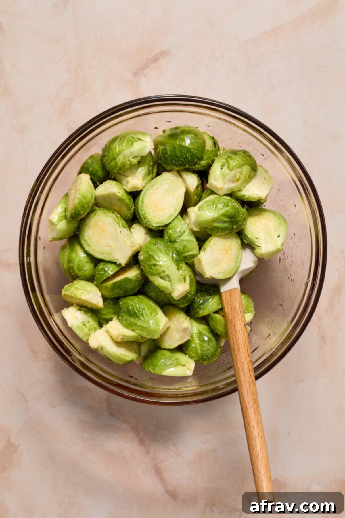 Brussels sprouts cut in half and tossed with oil and seasoning in a glass bowl, ready for the air fryer.