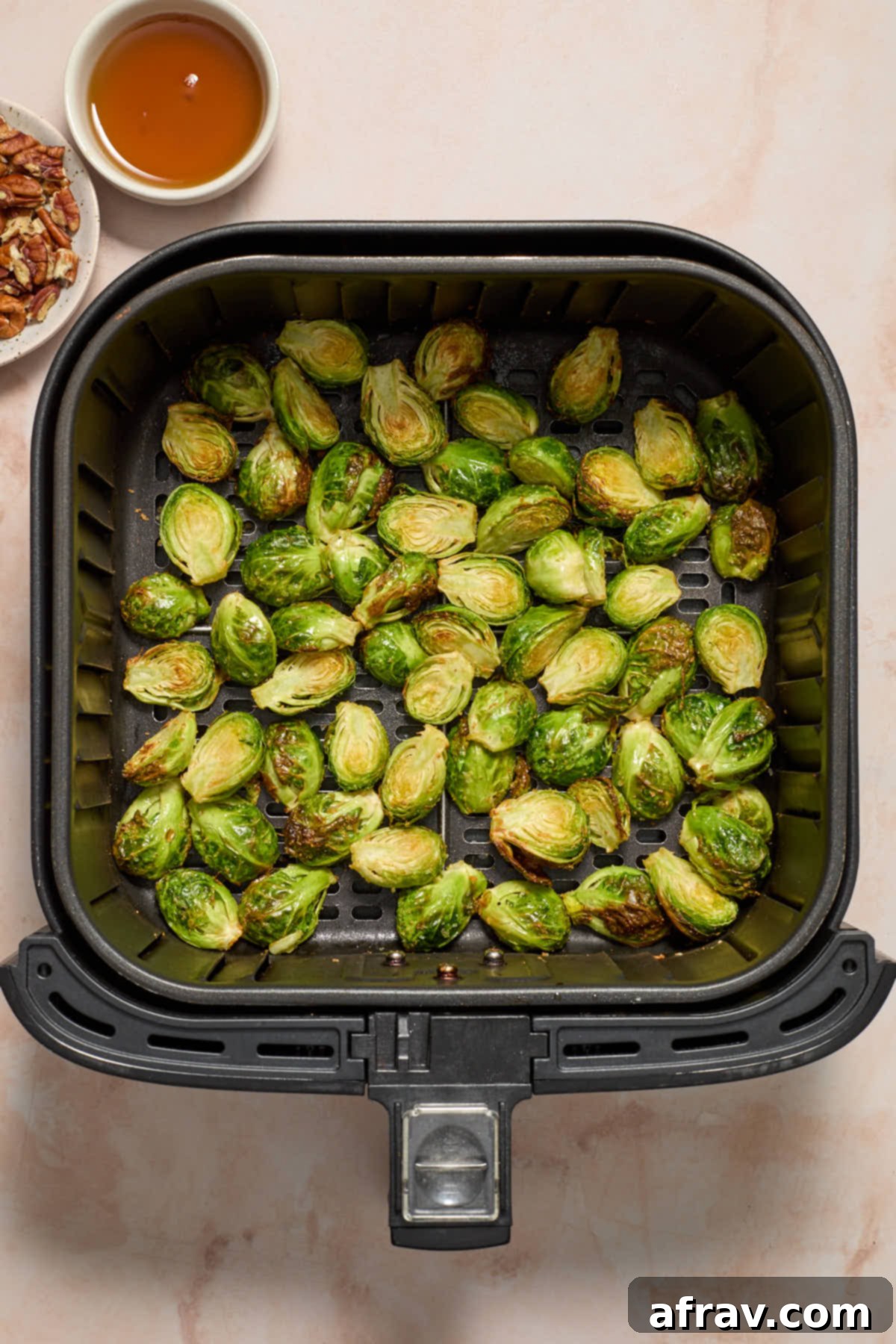 Partially air-fried Brussels sprouts in the basket, with pecans and maple syrup on the side, ready for the next step.