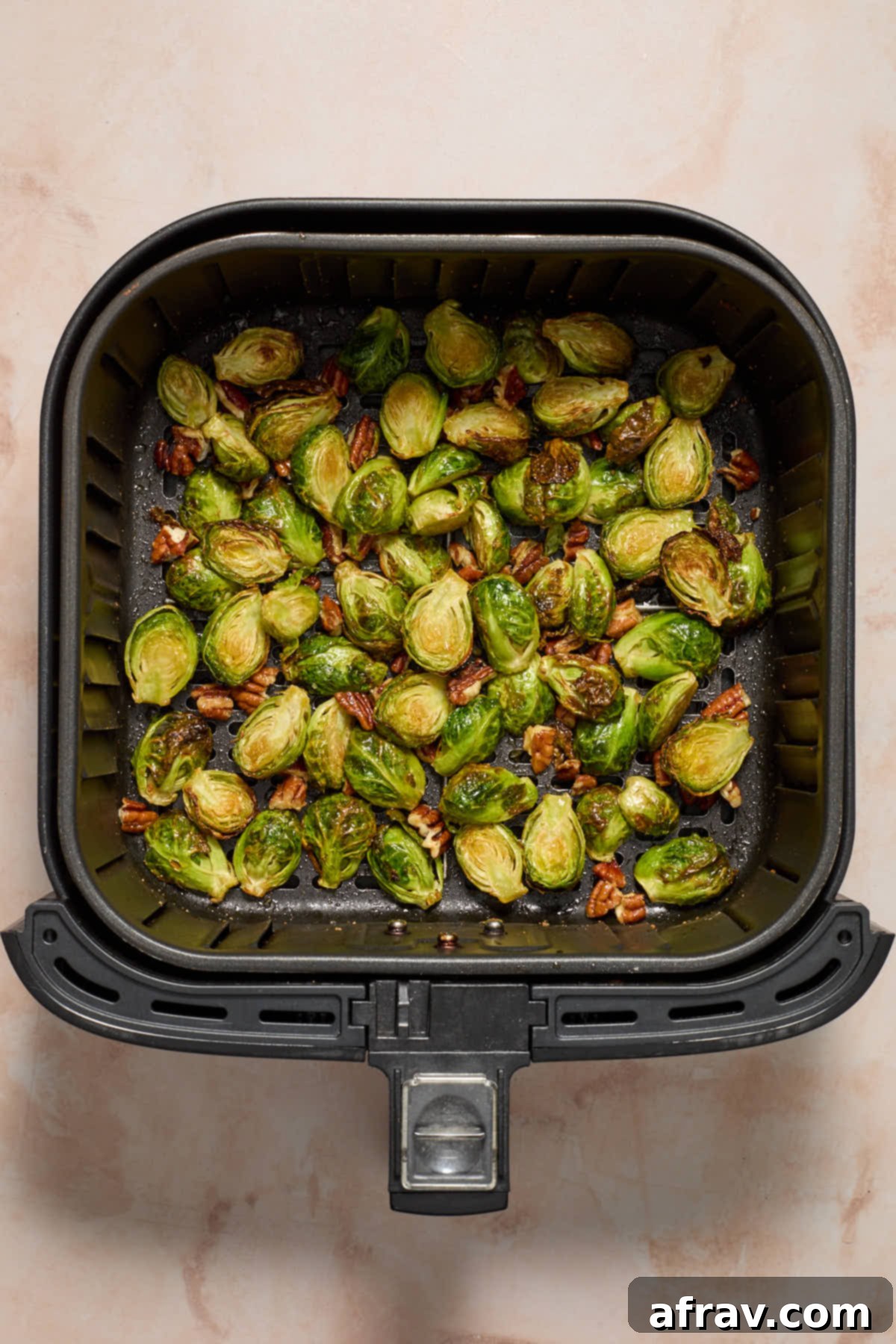 Maple pecan Brussels sprouts piled high in an air fryer basket, showing their crispy, caramelized texture.