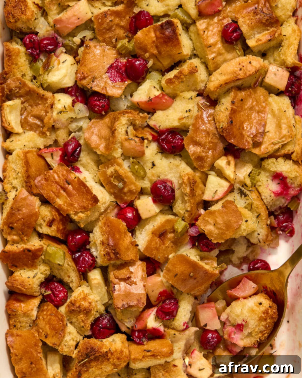Festive Apple Cranberry Stuffing 12 Close up of apple cranberry stuffing in a dish with a spoon inserted into it.