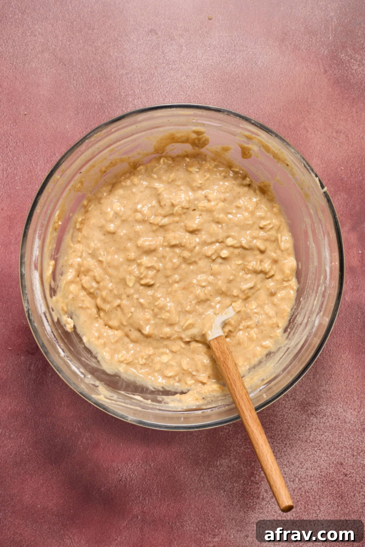 Muffin batter mixed together in a glass bowl with a spatula inserted into it.