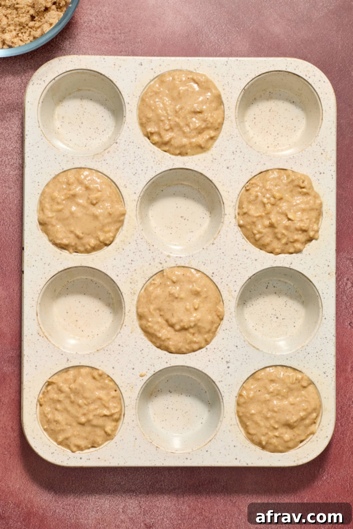 Batter spooned into every second muffin cup in a 12 cup muffin tin.