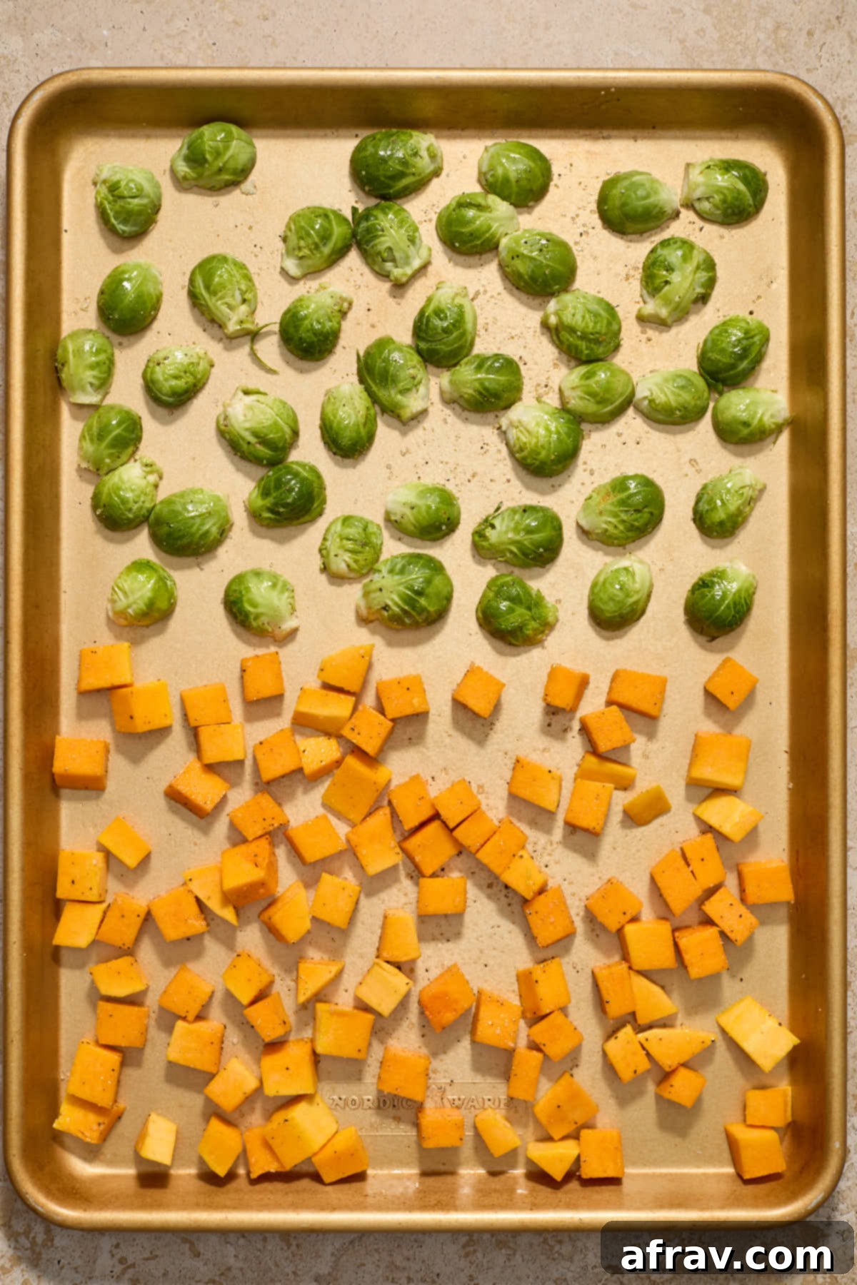 Cubed butternut squash and halved Brussels sprouts, seasoned and spread out on a baking sheet ready for roasting.