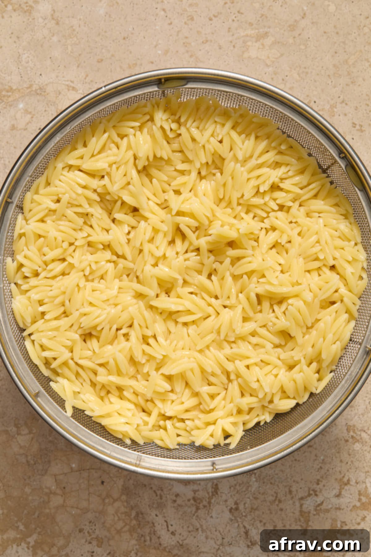 Cooked orzo pasta draining in a metal colander.