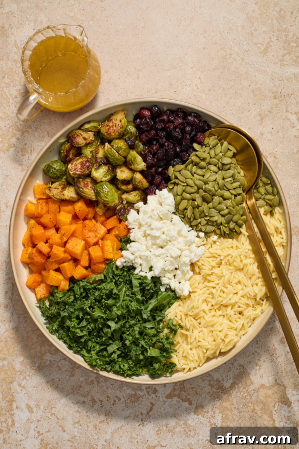 All of the orzo salad ingredients arranged in sections within a large, shallow bowl, with the vinaigrette served separately on the side.