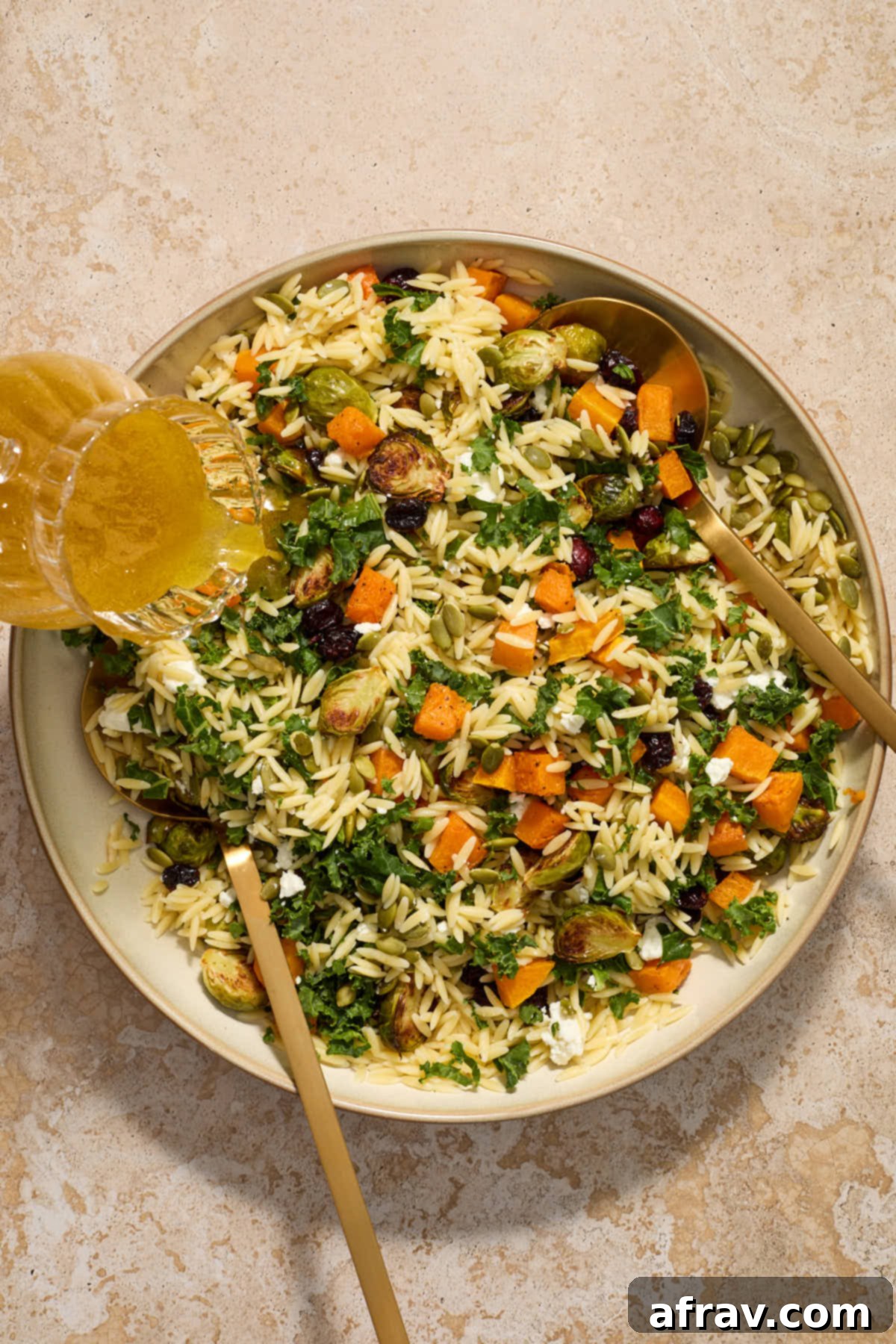 The orzo salad ingredients being tossed together in a bowl, with the apple cider vinaigrette being poured over the top.