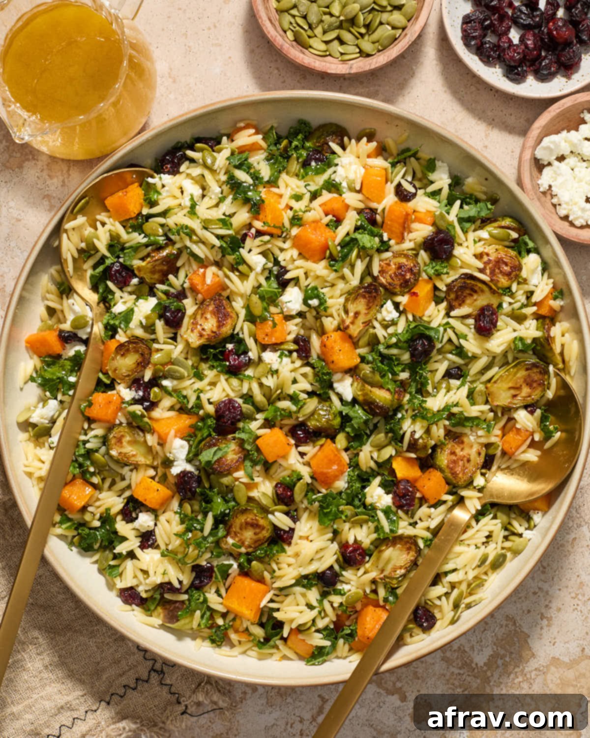 A close-up view of Fall Orzo Salad served in a large bowl, with serving spoons inserted for easy enjoyment.