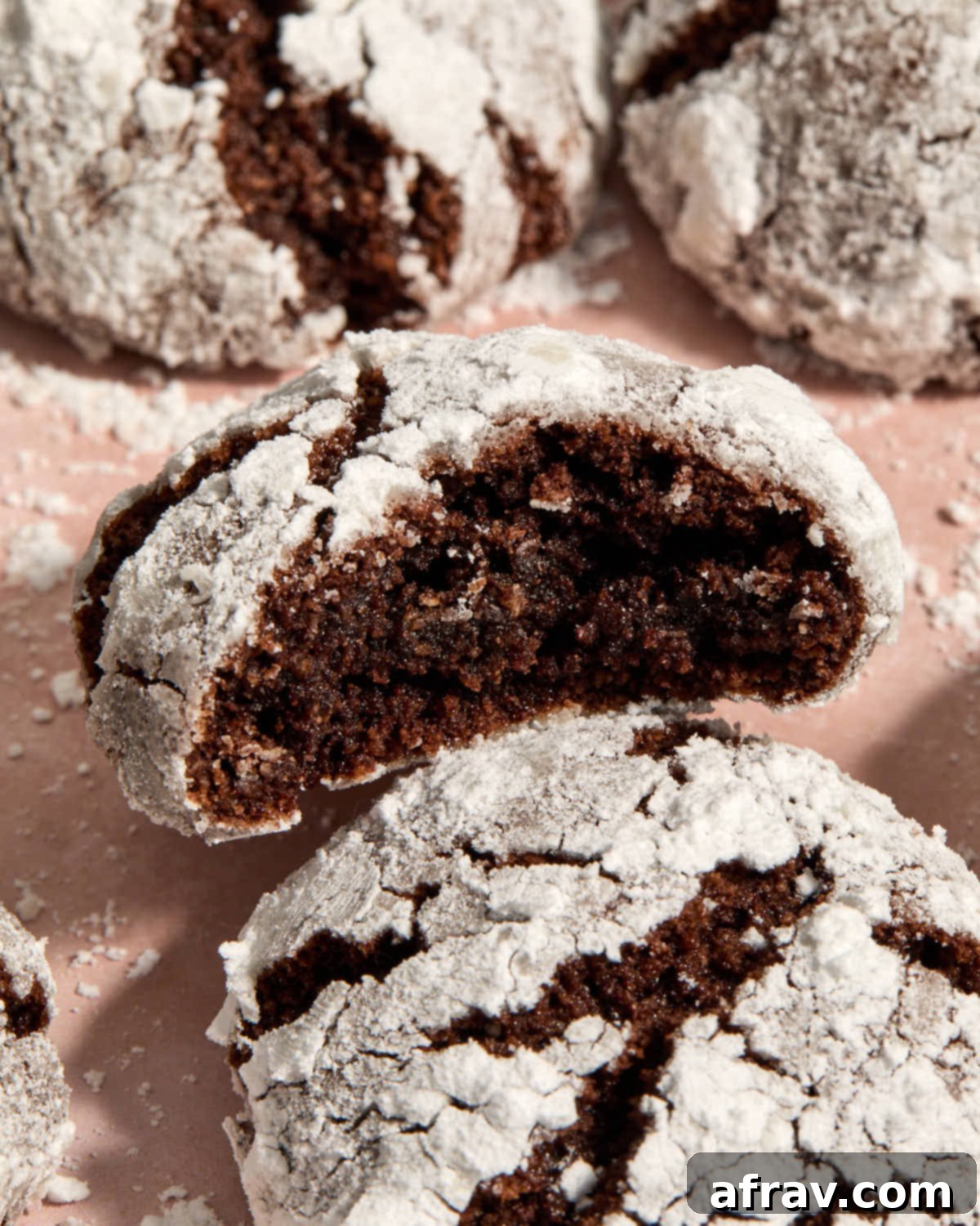 A close-up shot of an almond flour chocolate crinkle cookie with a bite taken out, resting on top of another cookie. The crackly texture and powdered sugar coating are clearly visible.