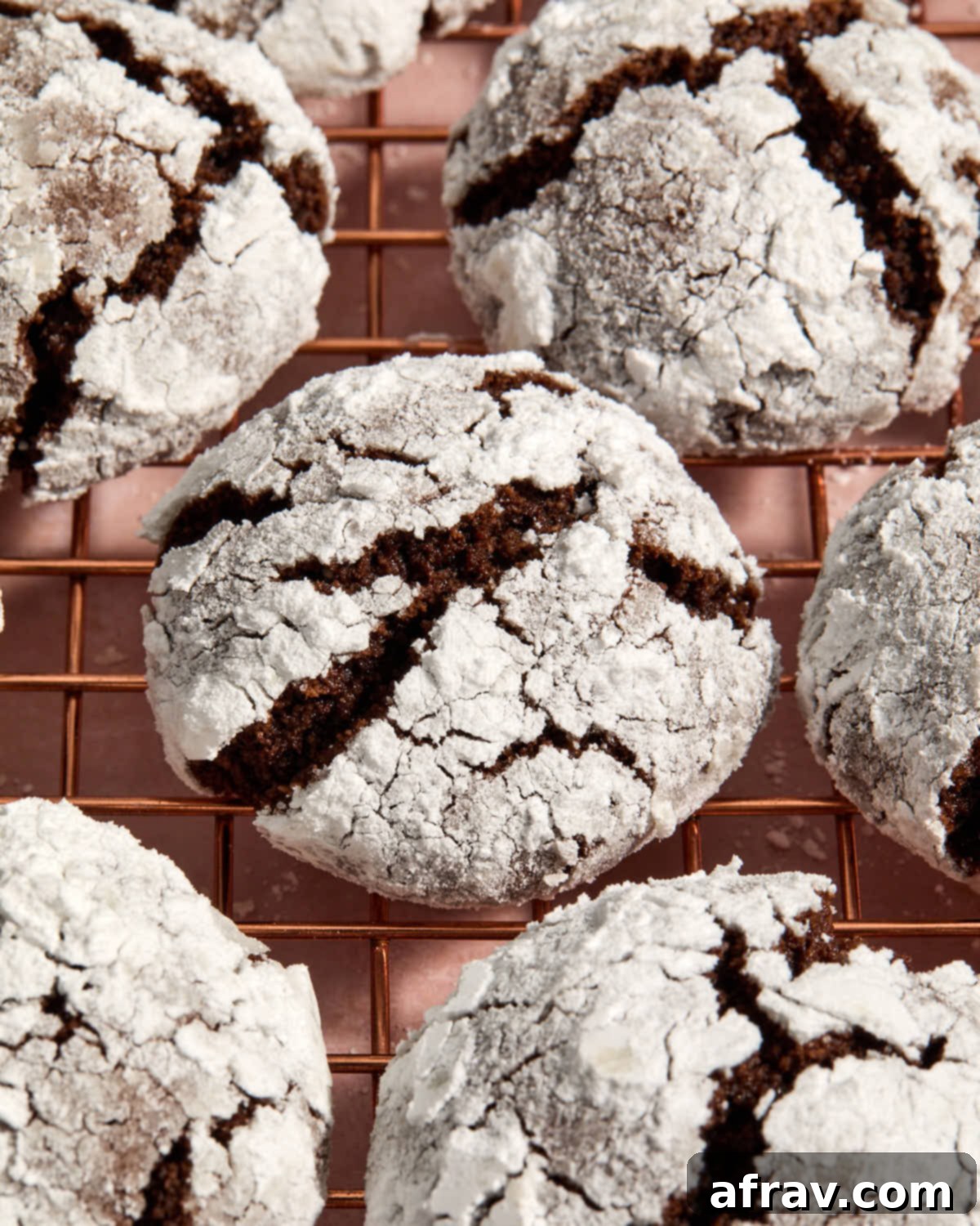 A close-up view of a perfectly baked almond flour chocolate crinkle cookie on a wire rack, highlighting its texture and powdered sugar coating.