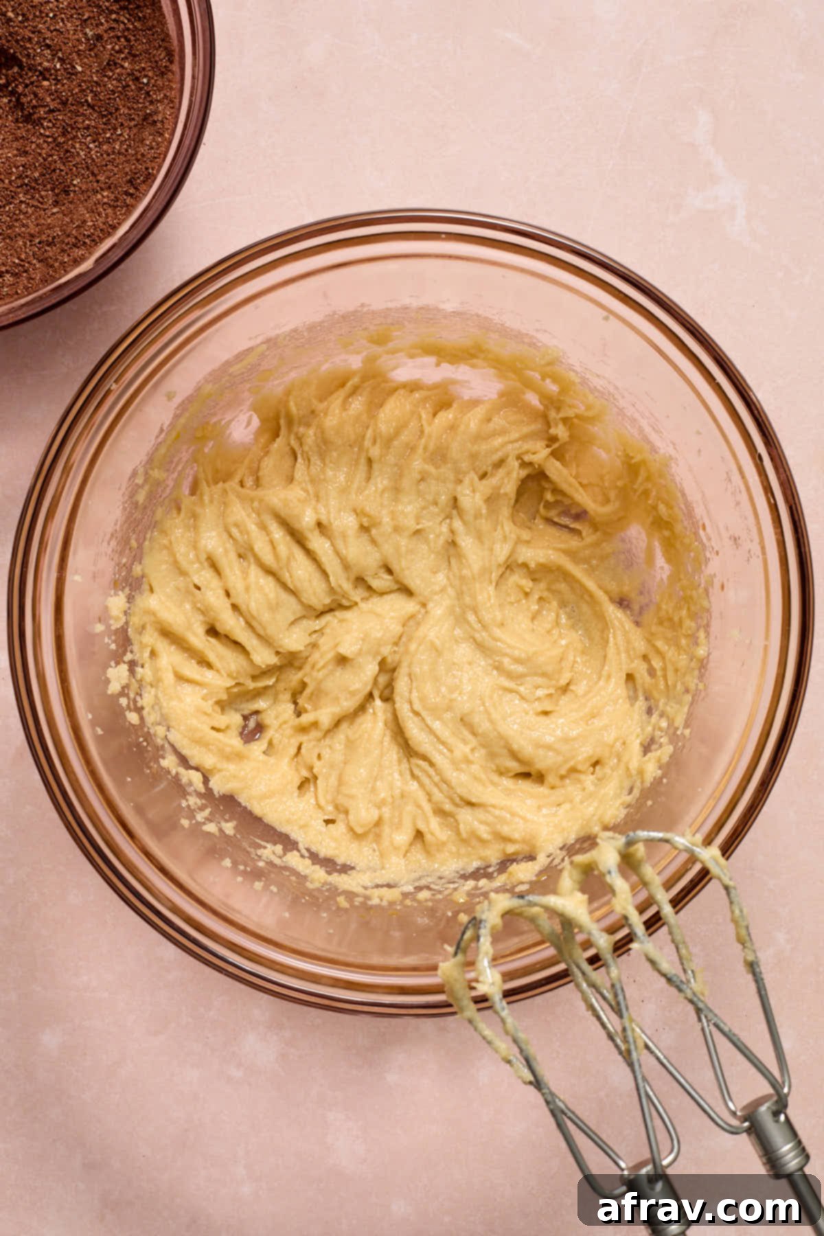 A glass bowl filled with wet ingredients perfectly mixed together, with a separate bowl of dry ingredients placed nearby, ready to be combined.
