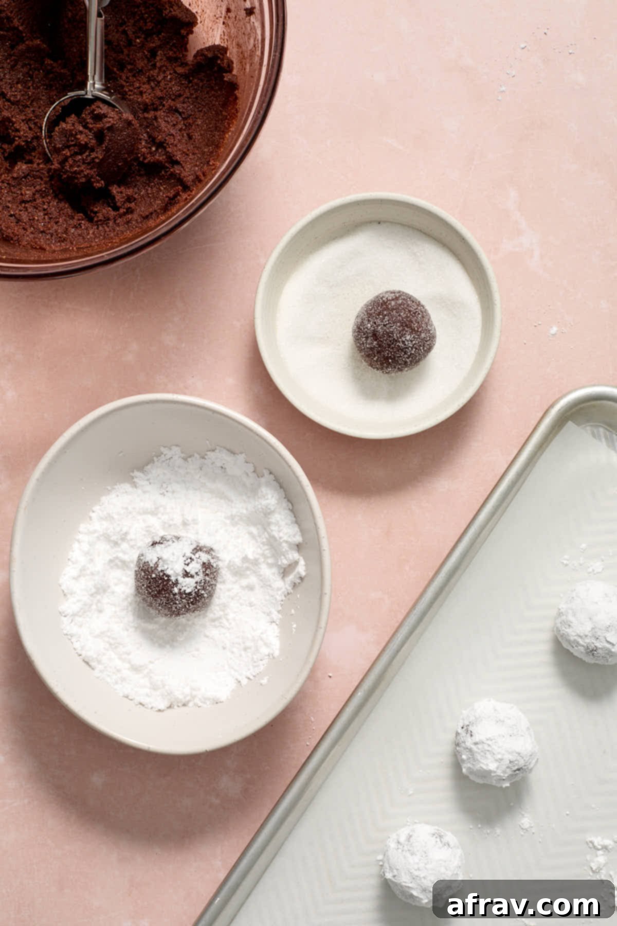 Cookie dough rolled into perfect balls, first coated in granulated sugar, and then generously covered in powdered sugar, ready for baking.