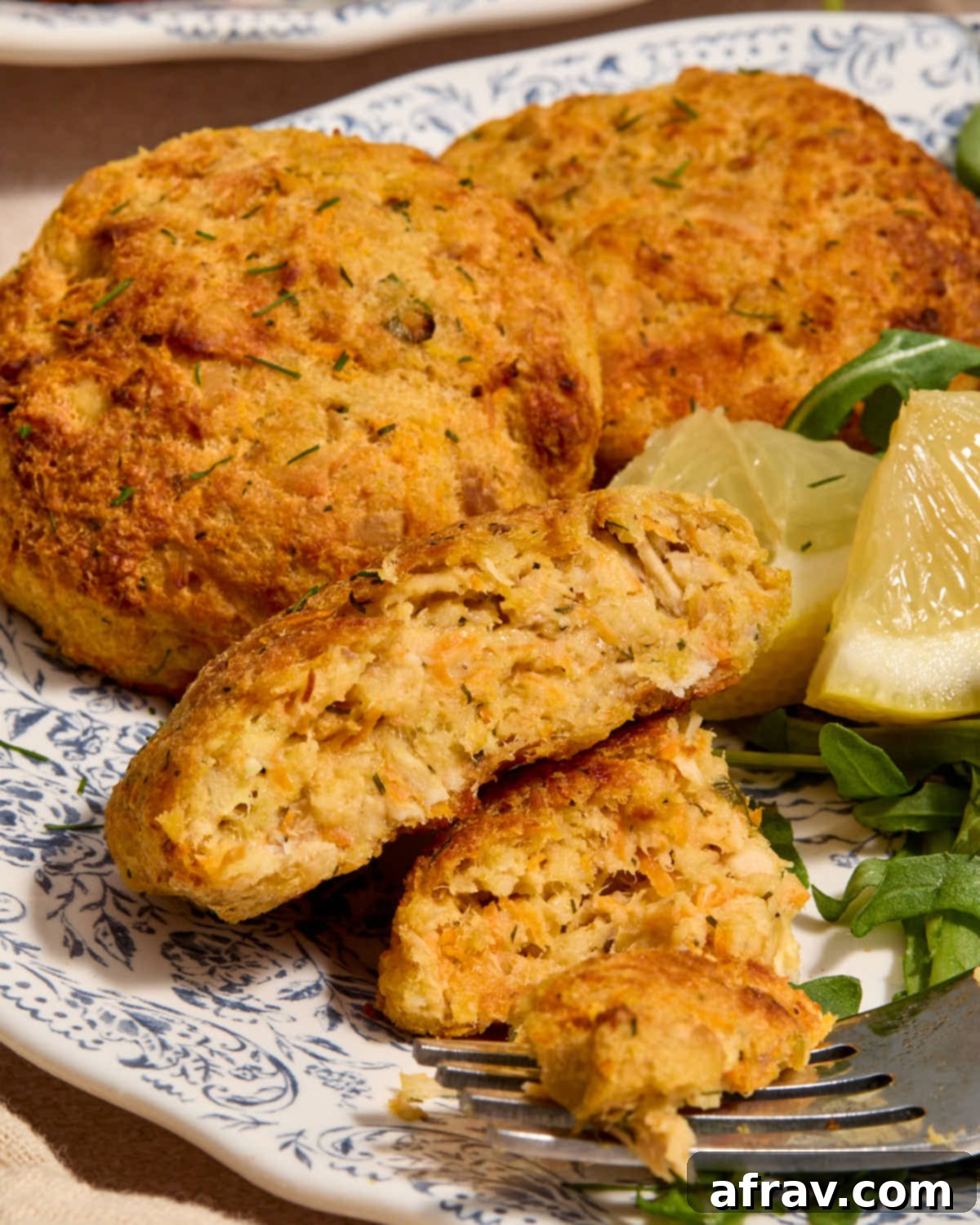 Air Fryer Tuna Cakes with Cheddar & Carrot Zest 2 Golden brown tuna cakes served on a plate, one cut in half revealing a soft interior.