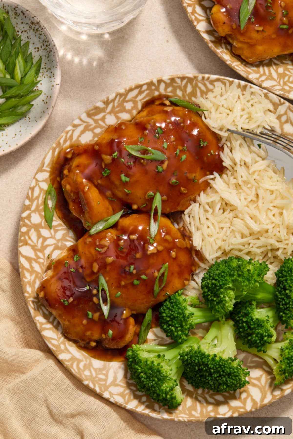 Honey Garlic Glazed Chicken Thighs: An Air Fryer Delight 2 Air fryer chicken thighs glazed with honey garlic sauce, plated with rice and broccoli, garnished with green onions.