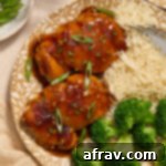 Air fryer boneless skinless chicken thighs coated in honey garlic sauce on a plate with green onion on top.